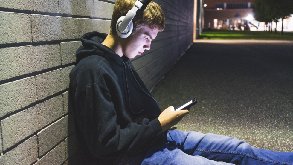 Young person sat on the floor wearing headphones and looking at phone
