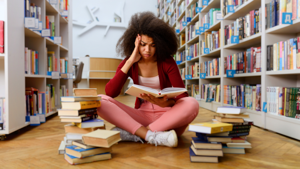 Stressed student sat in library with two piles of books