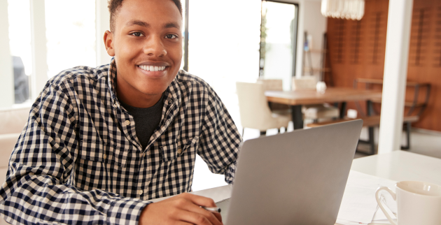 Young person sat using a laptop and smiling at the camera