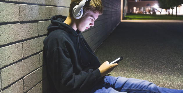 Young person sat on the floor wearing headphones and looking at phone