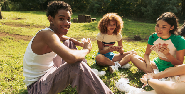 Three young people sat in a field playing cards