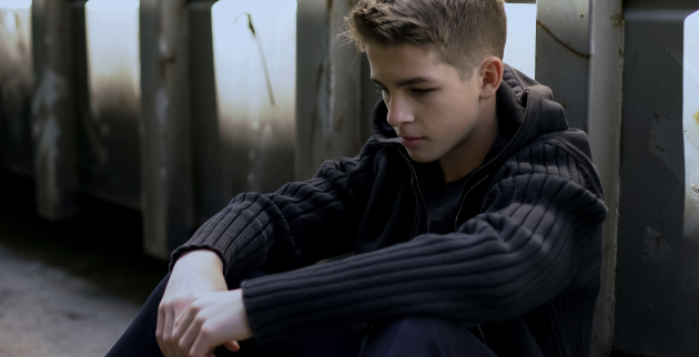 Sad looking young person sat down in dark alley