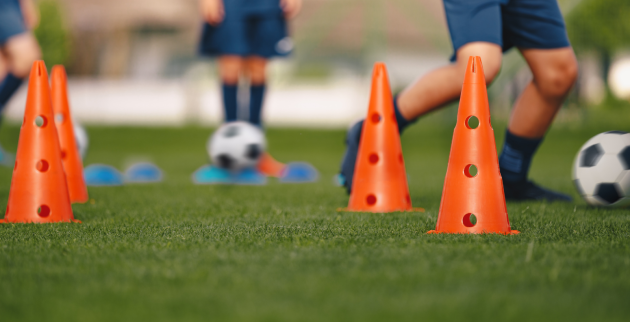 Three people kicking footballs around cones