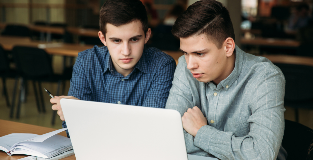 two students sat together using a laptop