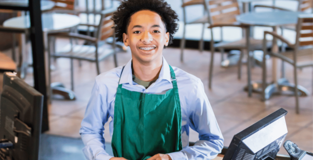 trainee at work stood at a till smiling at camera