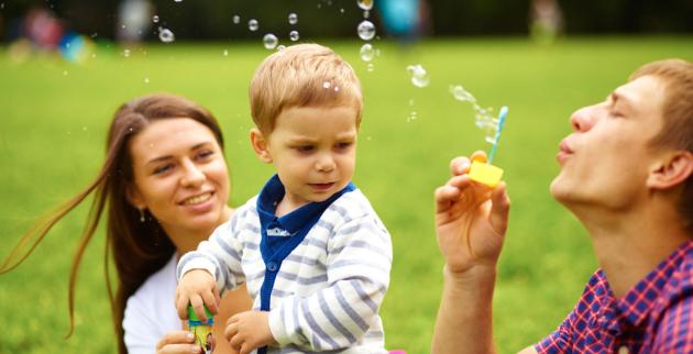 A young man and a young woman blow bubbles for a 1 year old child.