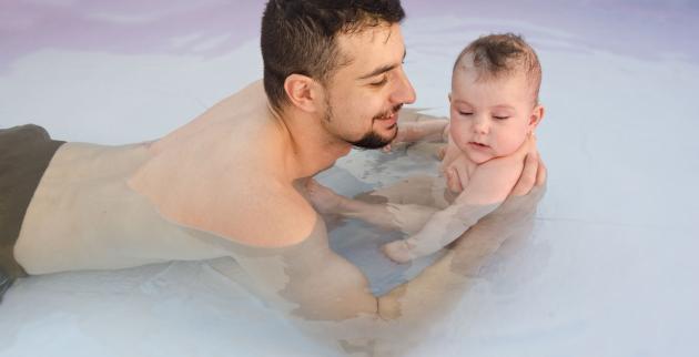 A young man in a swimming pool with a baby