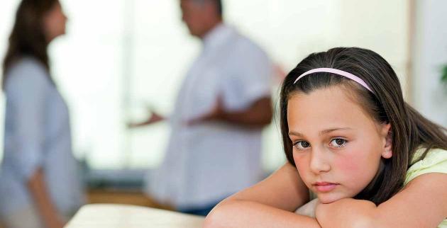 A girls leans on a table while her parents argue in the background