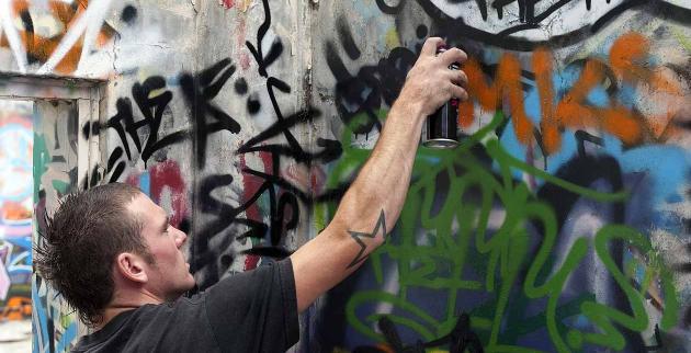 A Young Man sprays graffiti onto a wall