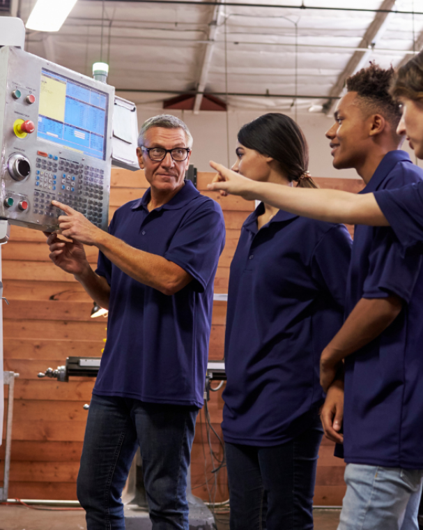 Three apprentices being shown how to use machine at work by manager