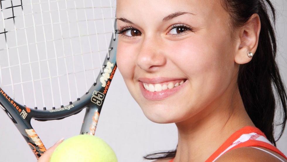 Young woman, smiling, holding a tennis racquet and tennis ball