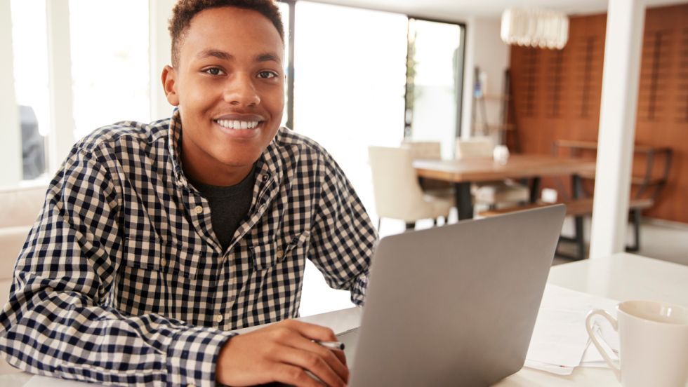 Young person sat using a laptop and smiling at the camera