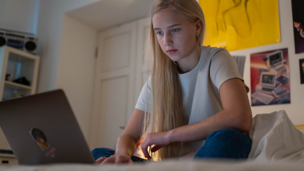 Young person sat on bed using laptop