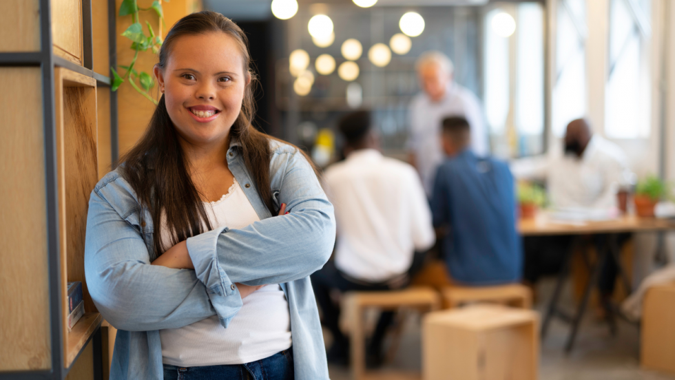 A young person looking at the camera and smiling, she has a learning disability