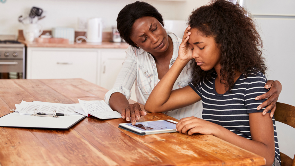 A young is sat at a table being comforted by their supporting adult