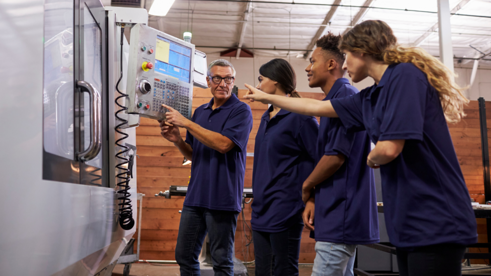 Three apprentices being shown how to use machine at work by manager