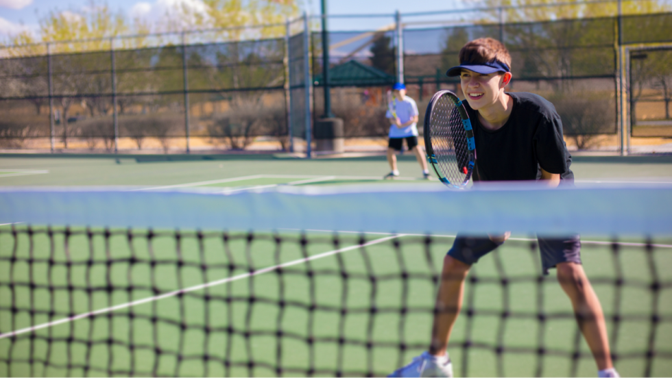 young person playing tennis outside