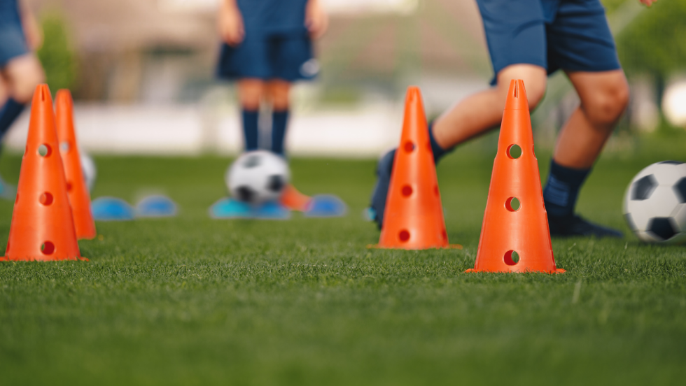 Three people kicking footballs around cones