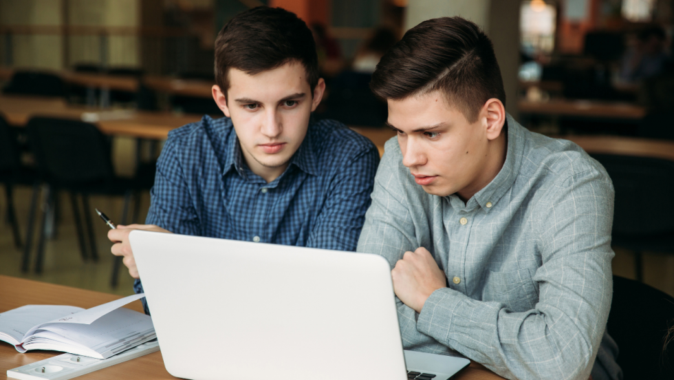 two students sat together using a laptop