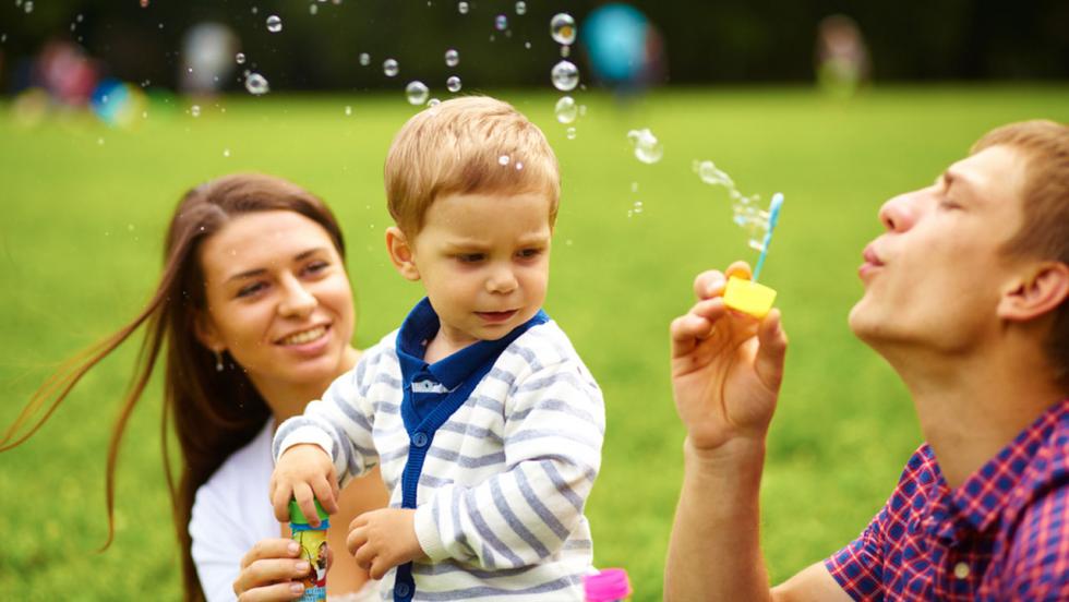 A young man and a young woman blow bubbles for a 1 year old child.