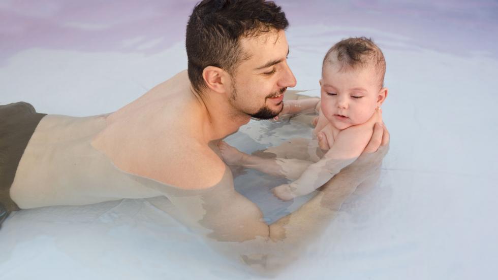 A young man in a swimming pool with a baby