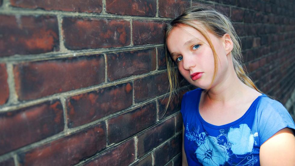 A sad looking girl leans against a brick wall