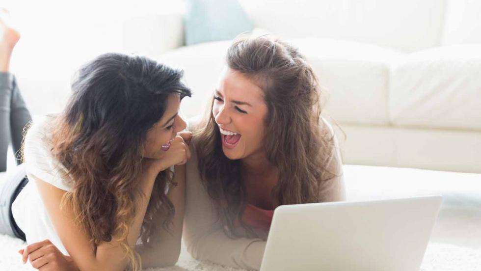 Two girls sharing a laptop and laughing
