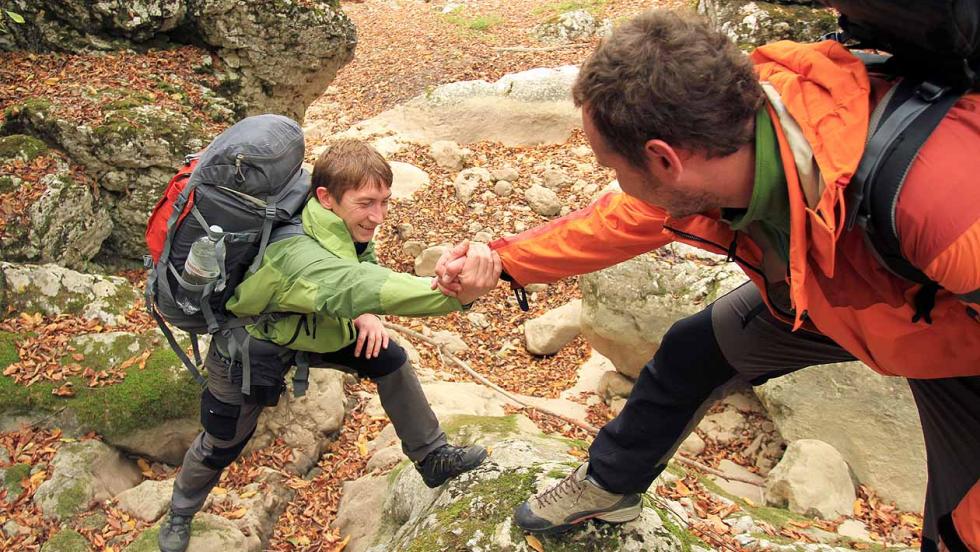 Two young men out walking, one helping the other climb a rocky slope