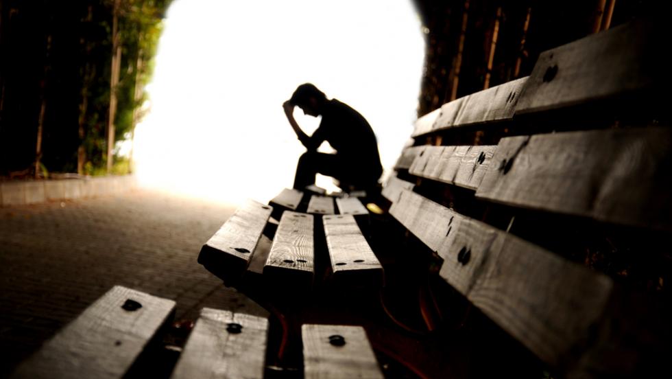 A young man sits in silhouette at the end of a tunnel