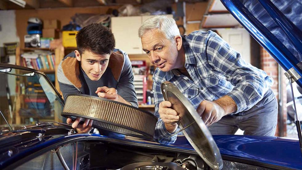 A young man and an older man work under the bonnet of a car