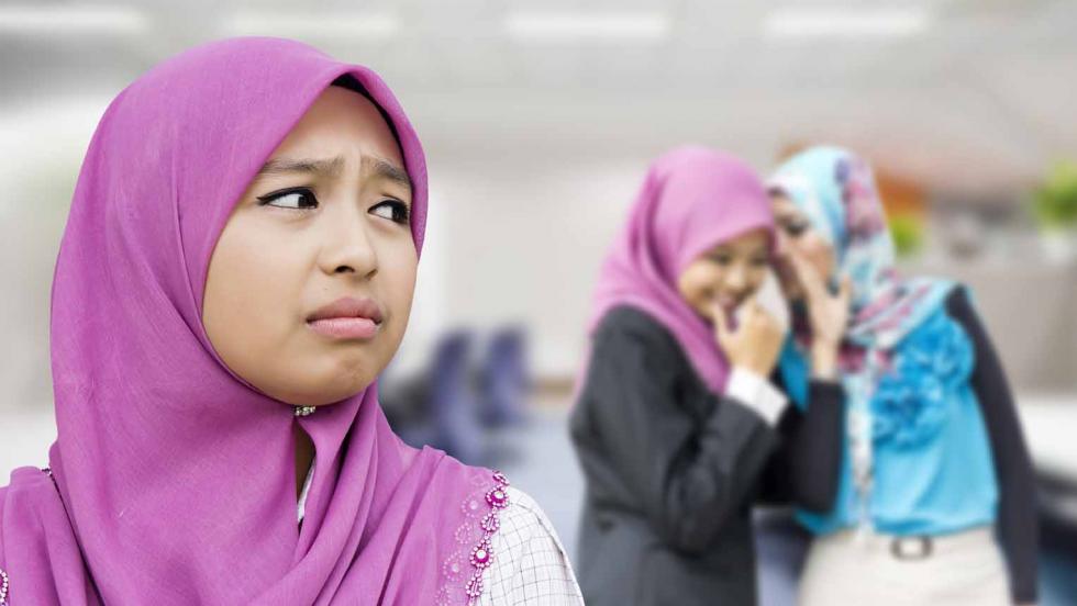 A girl in a headscarf looks sad while two other girls in headscarves giggle behind her