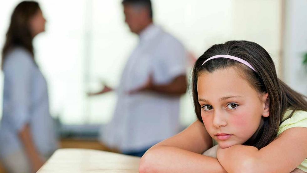 A girls leans on a table while her parents argue in the background