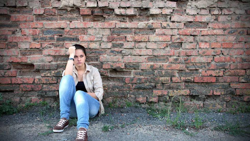 Young woman sat in front of a crumbling brick wall