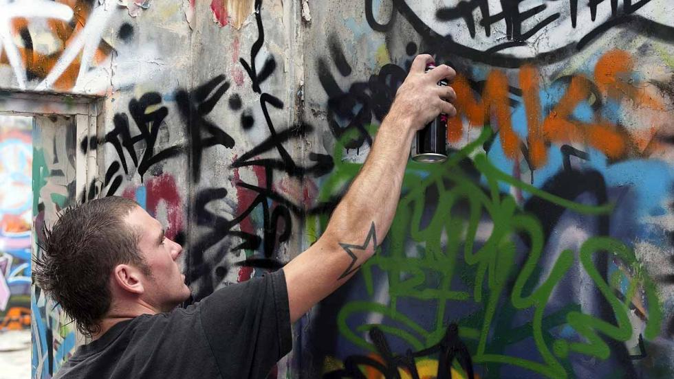 A Young Man sprays graffiti onto a wall