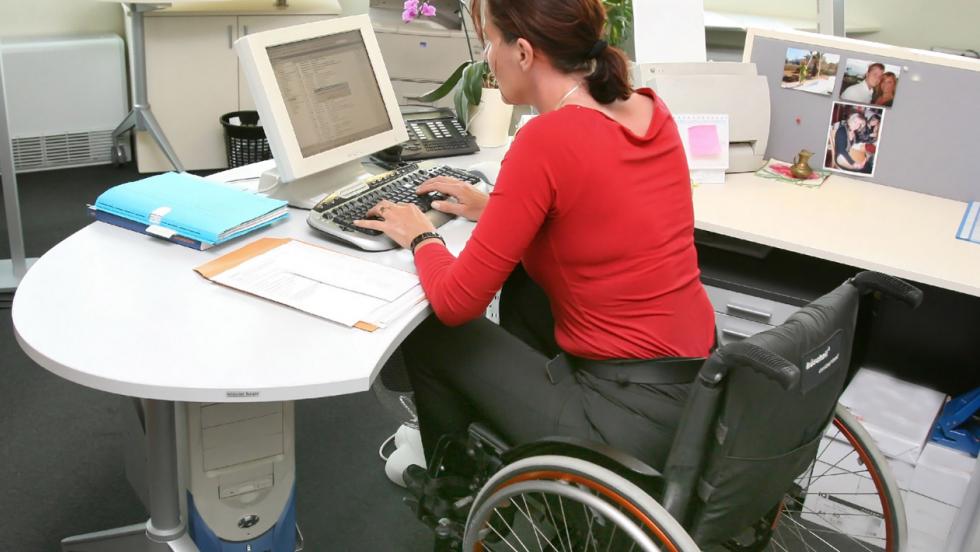 A woman in a wheelchair sits at an office desk