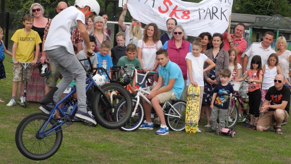 A young cyclist jumps a bike in front of a crowd of skate park supporters.