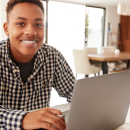 Young person sat using a laptop and smiling at the camera