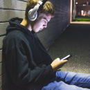 Young person sat on the floor wearing headphones and looking at phone
