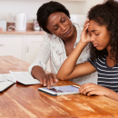 A young is sat at a table being comforted by their supporting adult