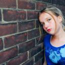 A sad looking girl leans against a brick wall