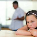 A girls leans on a table while her parents argue in the background