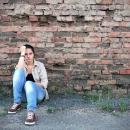 Young woman sat in front of a crumbling brick wall