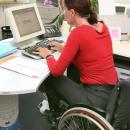 A woman in a wheelchair sits at an office desk